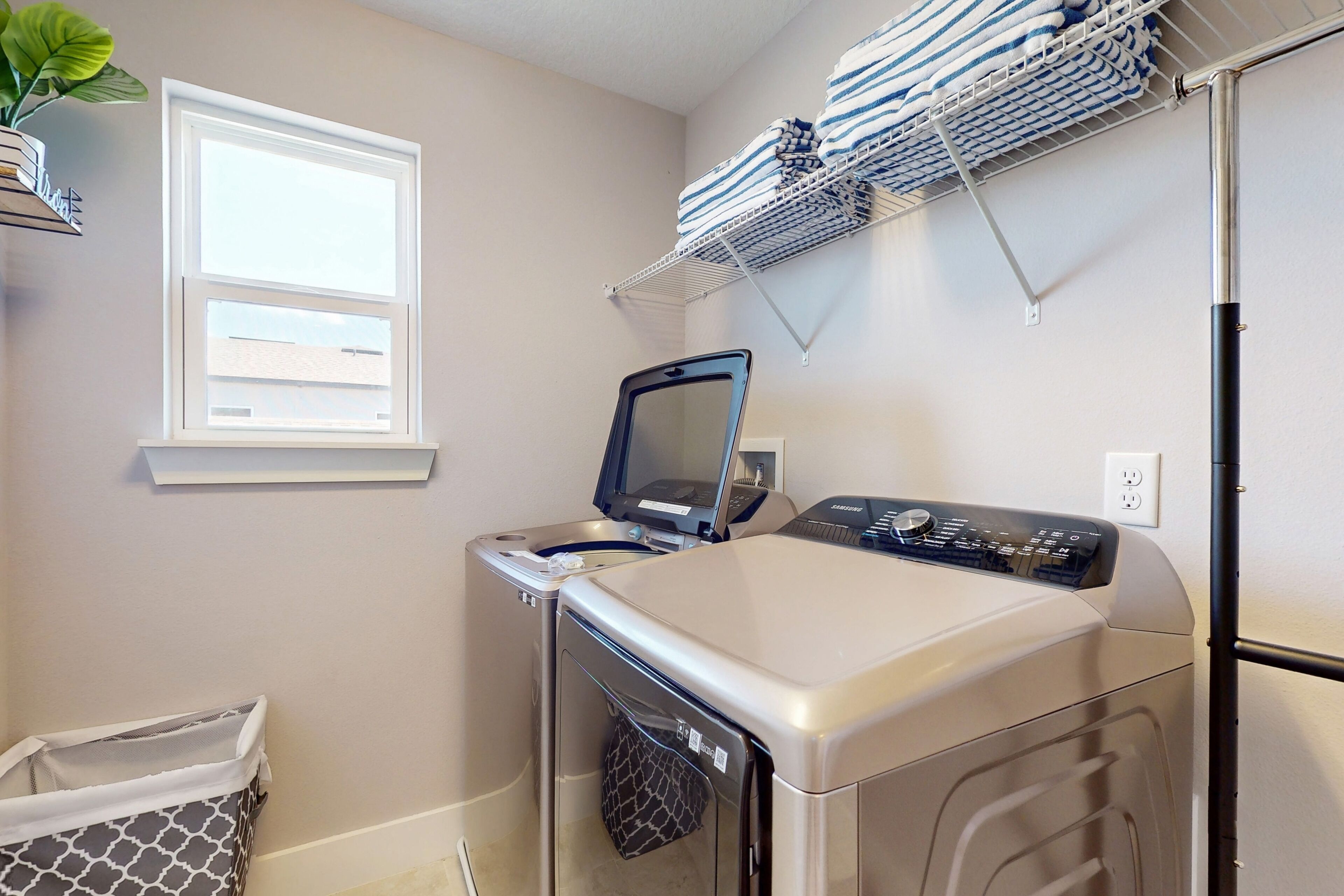 A laundry area with a front-loading washer and dryer, a window, and a shelf with folded towels.