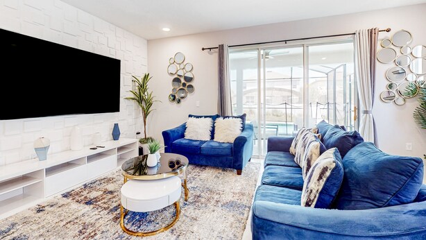 A modern living room with a large flat-screen TV, blue sofas, a white entertainment unit, and a patterned rug. - Bright Home With Private Pool, Washer/dryer and Internet (Kissimmee)