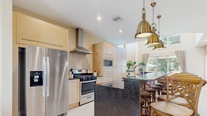 A modern kitchen with stainless steel appliances, a central island, wooden chairs, and a large window. - Beautiful Home With Resort Pool and Space for the Whole Family (Kissimmee)