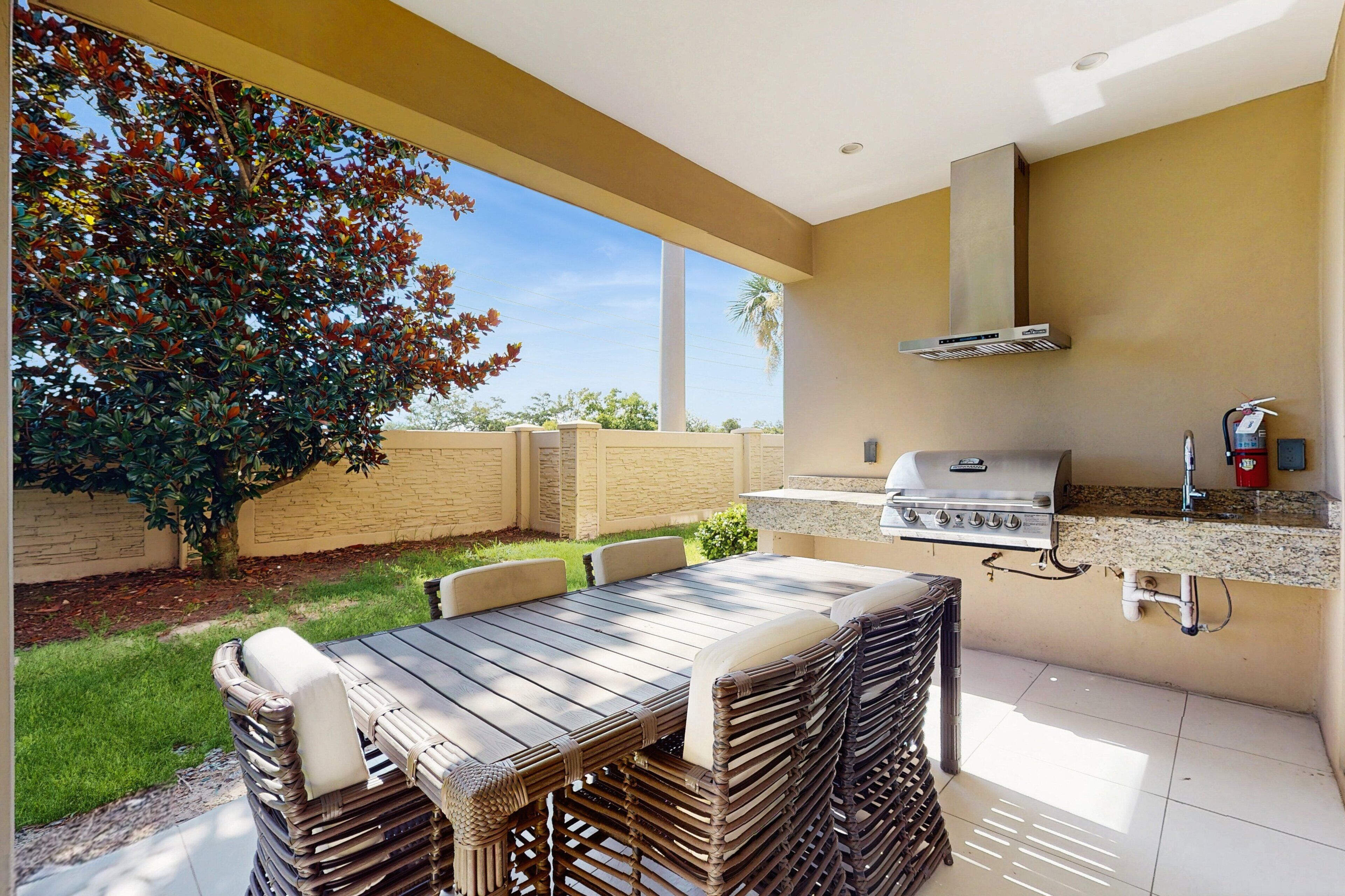 Cucina esterna con barbecue, tavolo da pranzo e sedie, immersa in un giardino e circondata da un muro in mattoni.