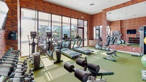A gym with exercise equipment, large windows, and a brick wall. - Beautiful Home With Resort Pool and Space for the Whole Family (Kissimmee)