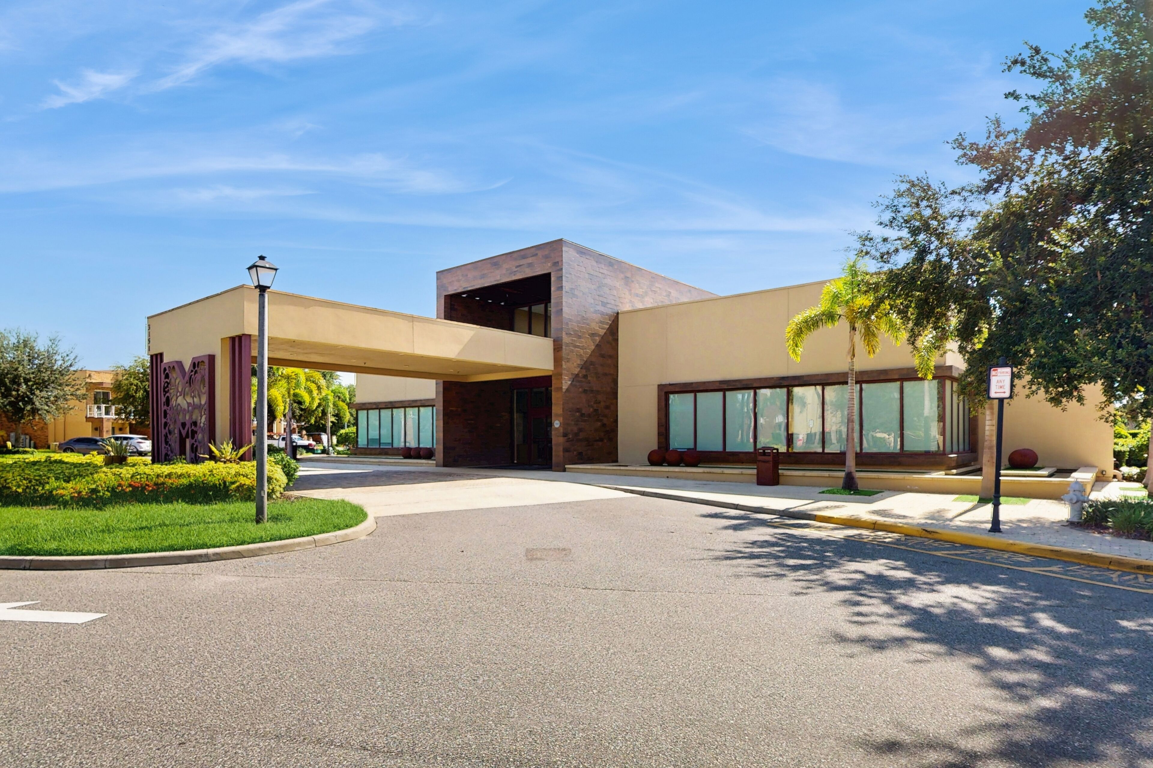 A modern building with a central entrance, large windows, and a landscaped area with trees and a pathway.