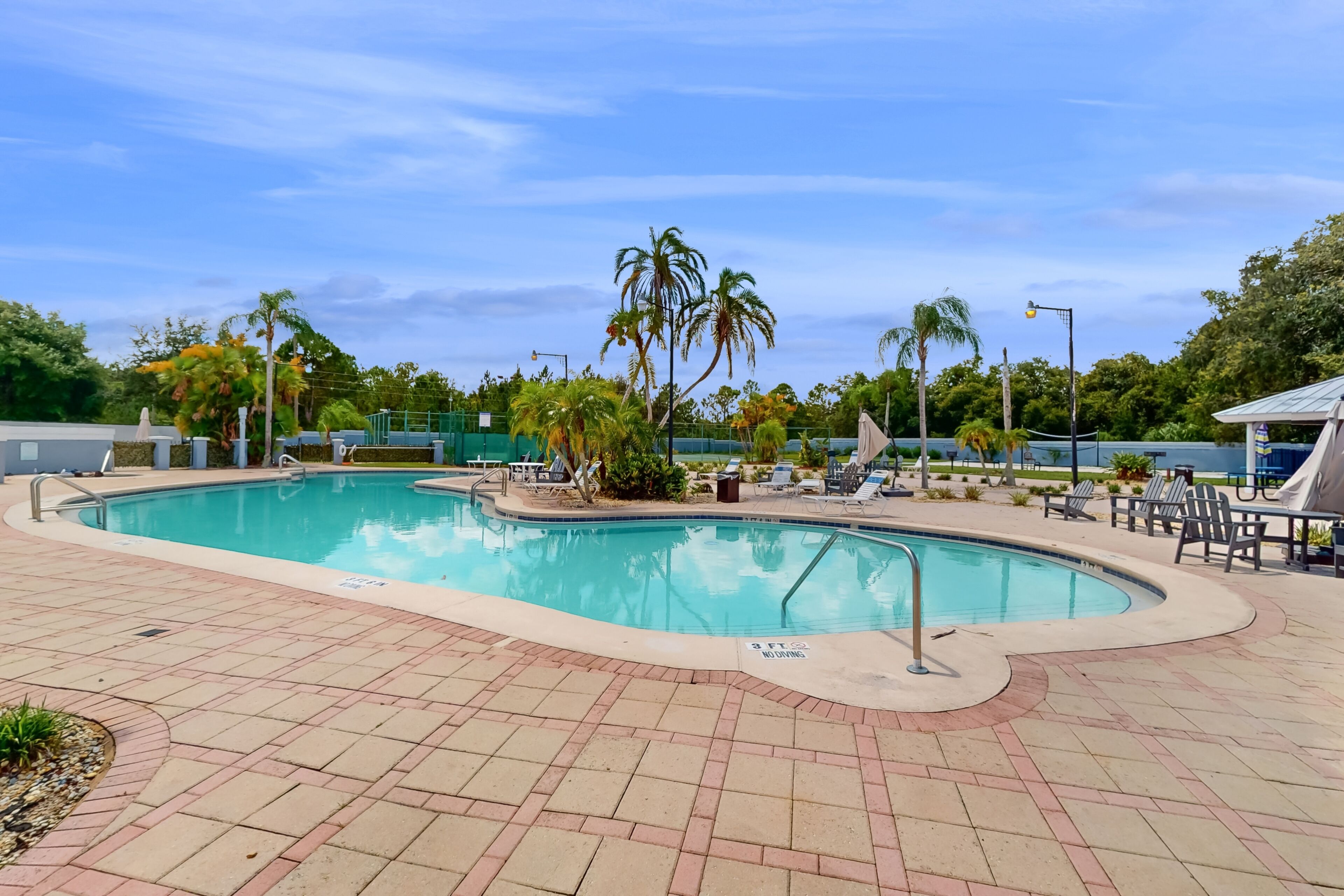 A swimming pool with a tiled deck, palm trees, and lounge chairs.