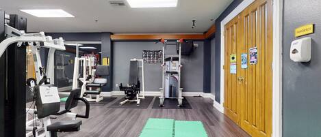 Un gimnasio con equipo de ejercicio, colchonetas verdes y una puerta de madera con la leyenda 'Aerobics'.