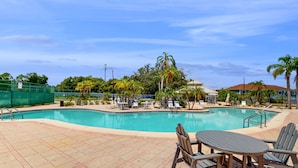 A swimming pool with lounge chairs and a table, surrounded by palm trees and a clear sky. - Comfortable Townhome Near Disney With Athletic Courts & Pool Access, Patio, & AC (Davenport)