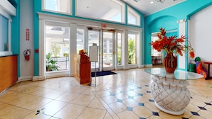 A hotel lobby with a reception desk, a glass-top table with a decorative vase, a fire extinguisher, and a blue exit sign. - Comfortable Townhome Near Disney With Athletic Courts & Pool Access, Patio, & AC (Davenport)