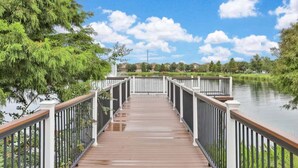 A wooden bridge with white railings leading to a body of water, surrounded by greenery and houses in the background. - Beautiful Home With Private Pool and Space for the Whole Family (Kissimmee)