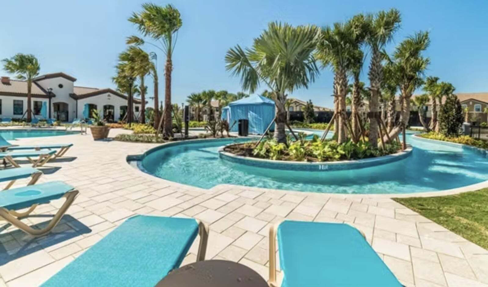 A pool area with lounge chairs, palm trees, and a blue tent.