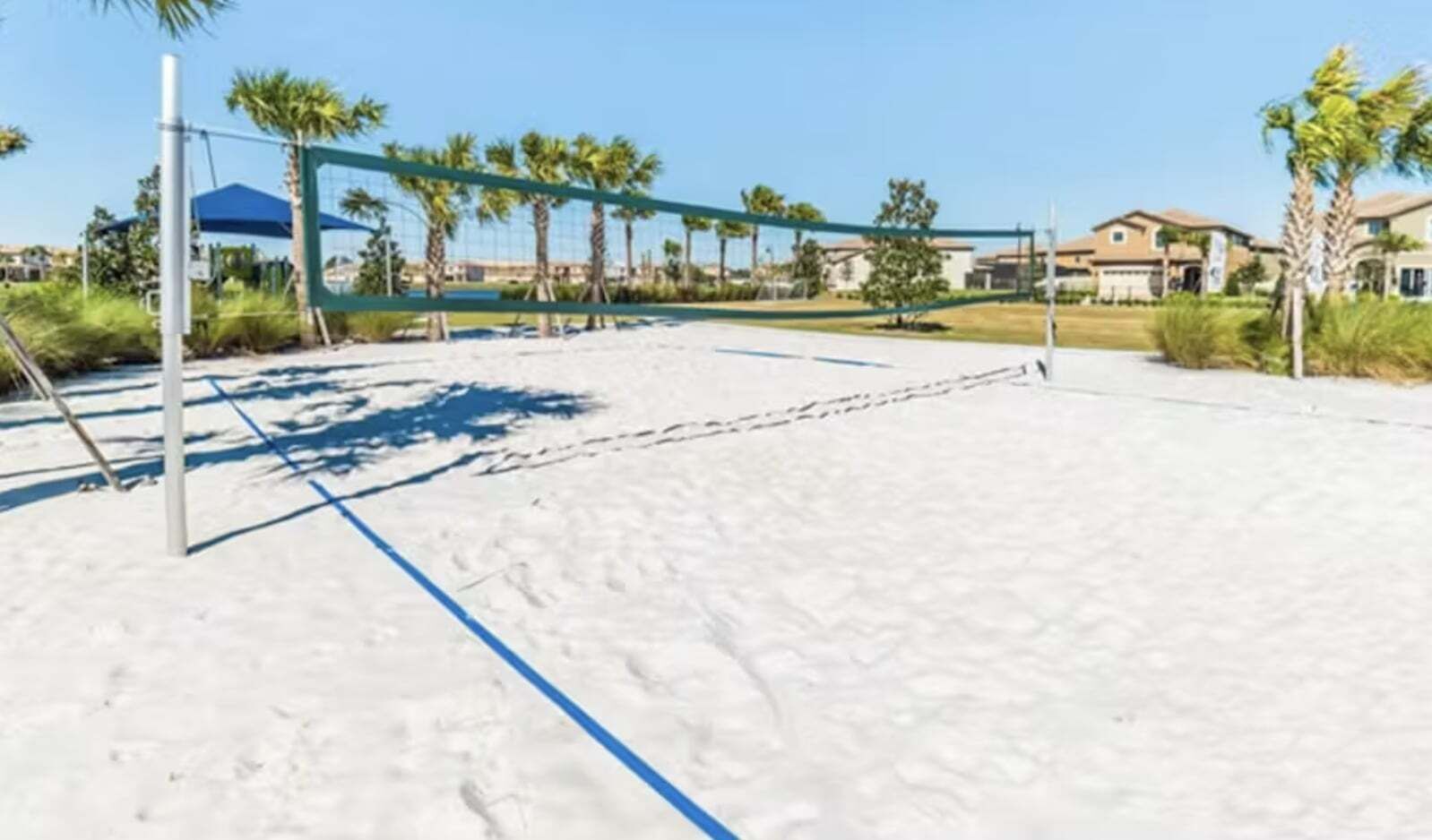 En strandvolleybane med net, omgivet af palmer og huse.