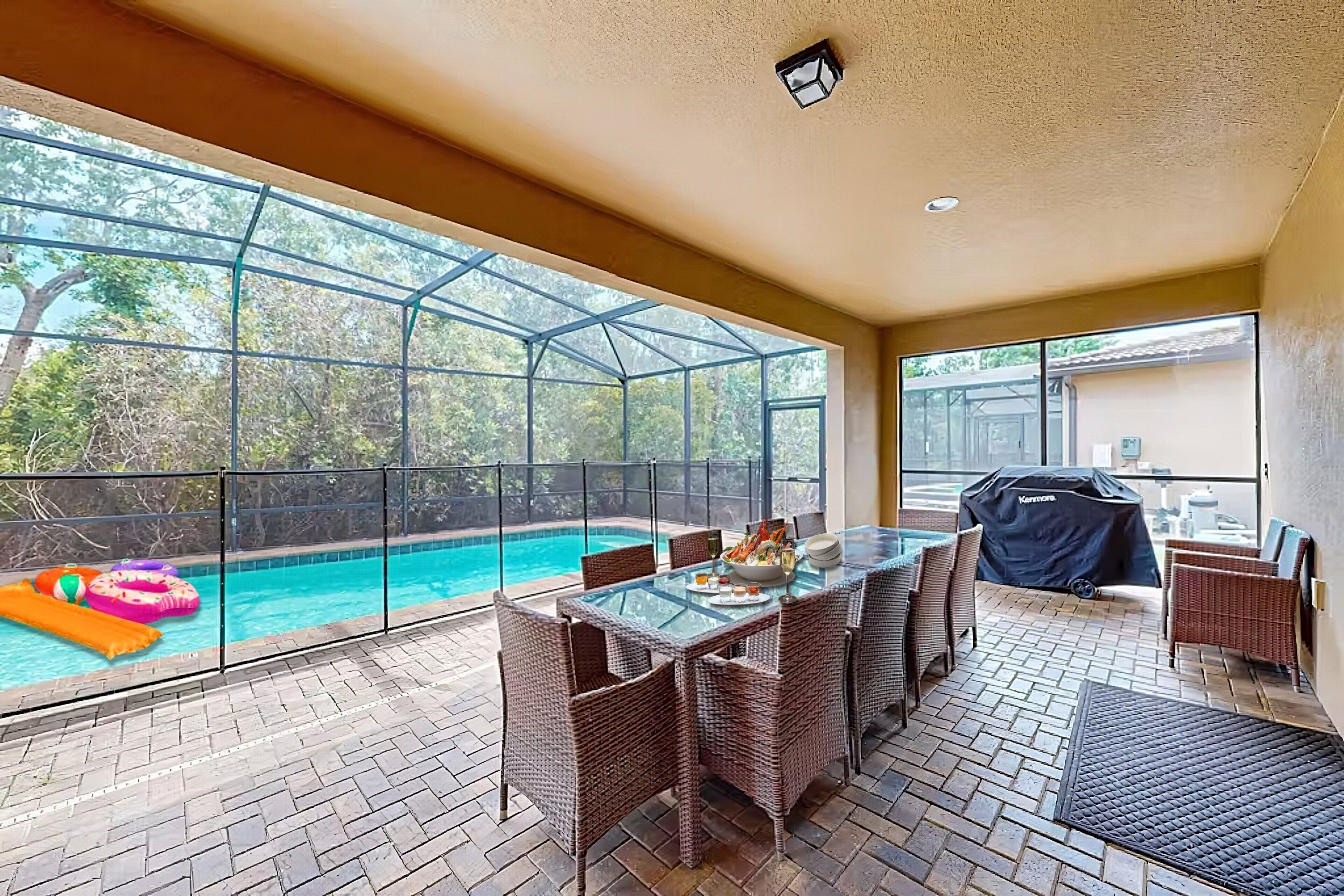 Une terrasse couverte avec une table en verre, des chaises en osier et une vue sur une piscine.