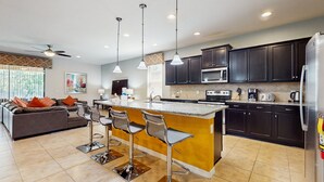 A modern kitchen with dark cabinets, a central island with bar stools, a microwave, and a refrigerator. - Beautiful Home With Private Pool and Space for the Whole Family (Kissimmee)
