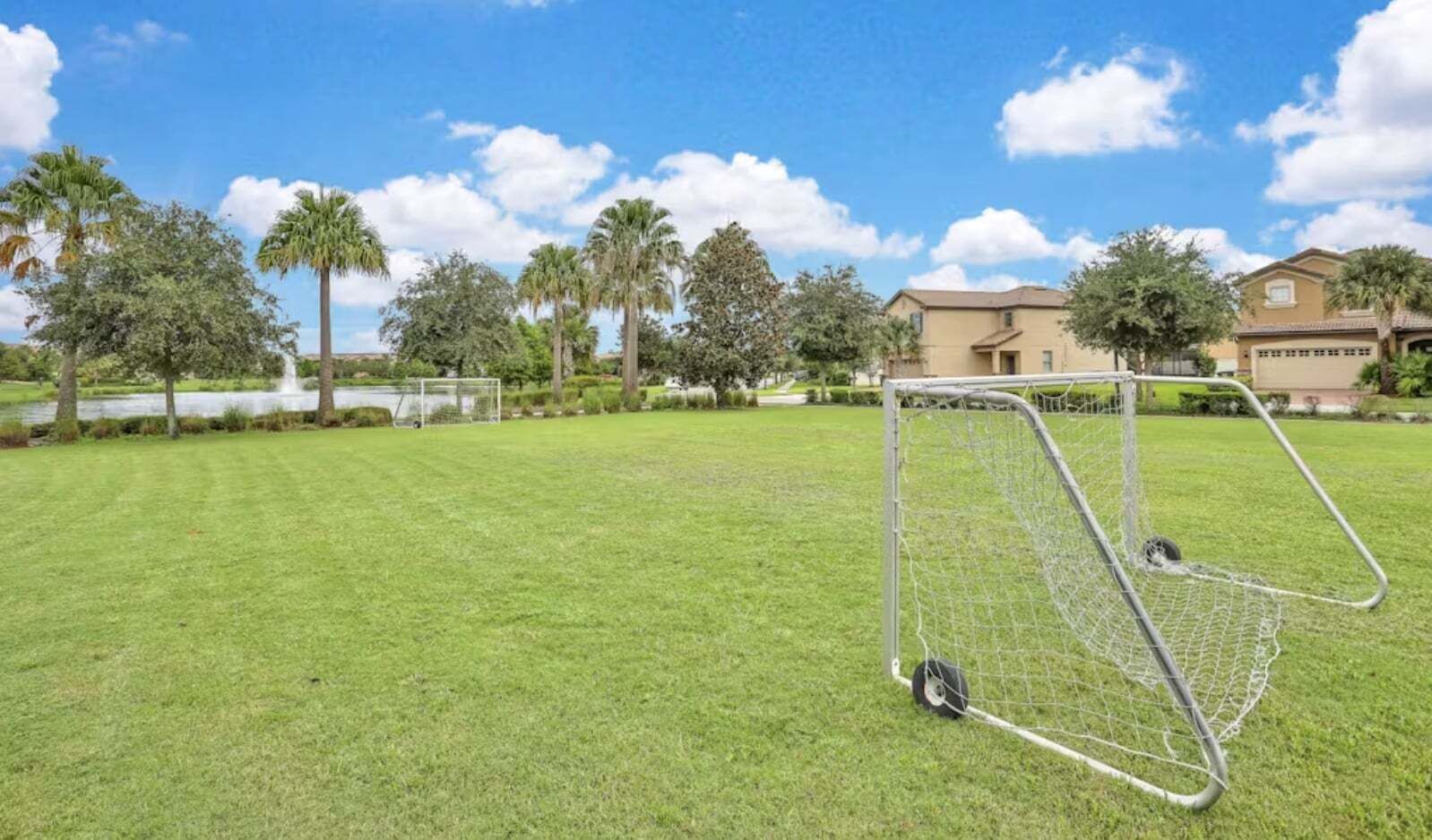 Un campo cubierto de hierba con un arco de fútbol, palmeras y un edificio al fondo.