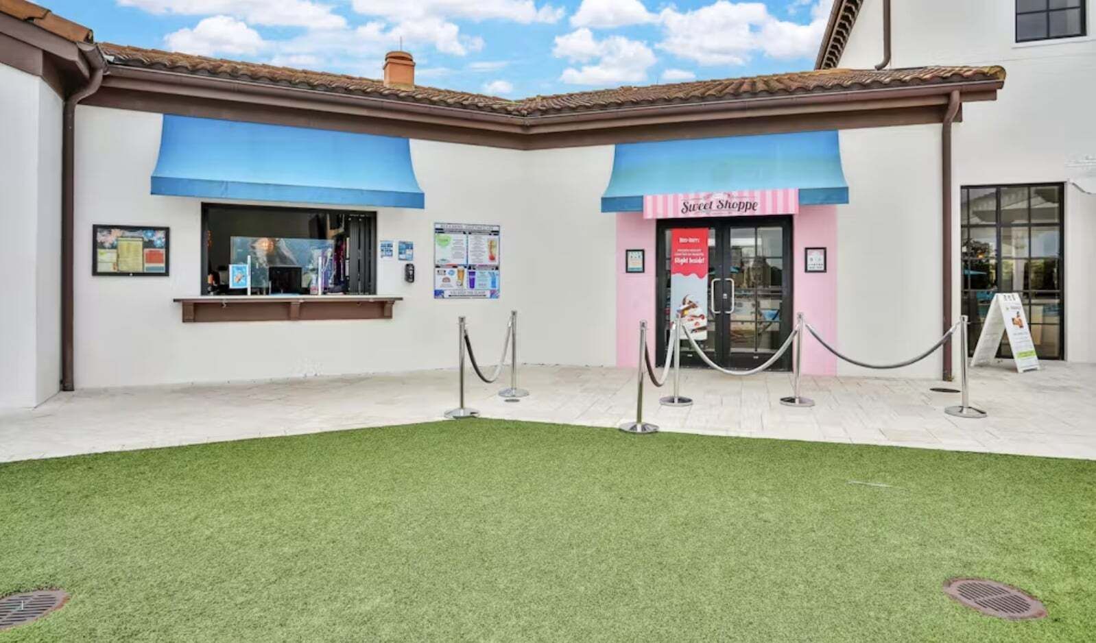 Ein Geb äude mit einer blauen Markise, einem Schild mit der Aufschrift 'Sweet Shoppe' und einem grünen Rasen aus Kunststoff.