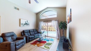 A living room with a sofa, a glass coffee table, a ceiling fan, a large window with curtains, and a view of a pool. - Private Pool Home With Spa, Screened Patio, Central AC, & Washer/dryer (Davenport)