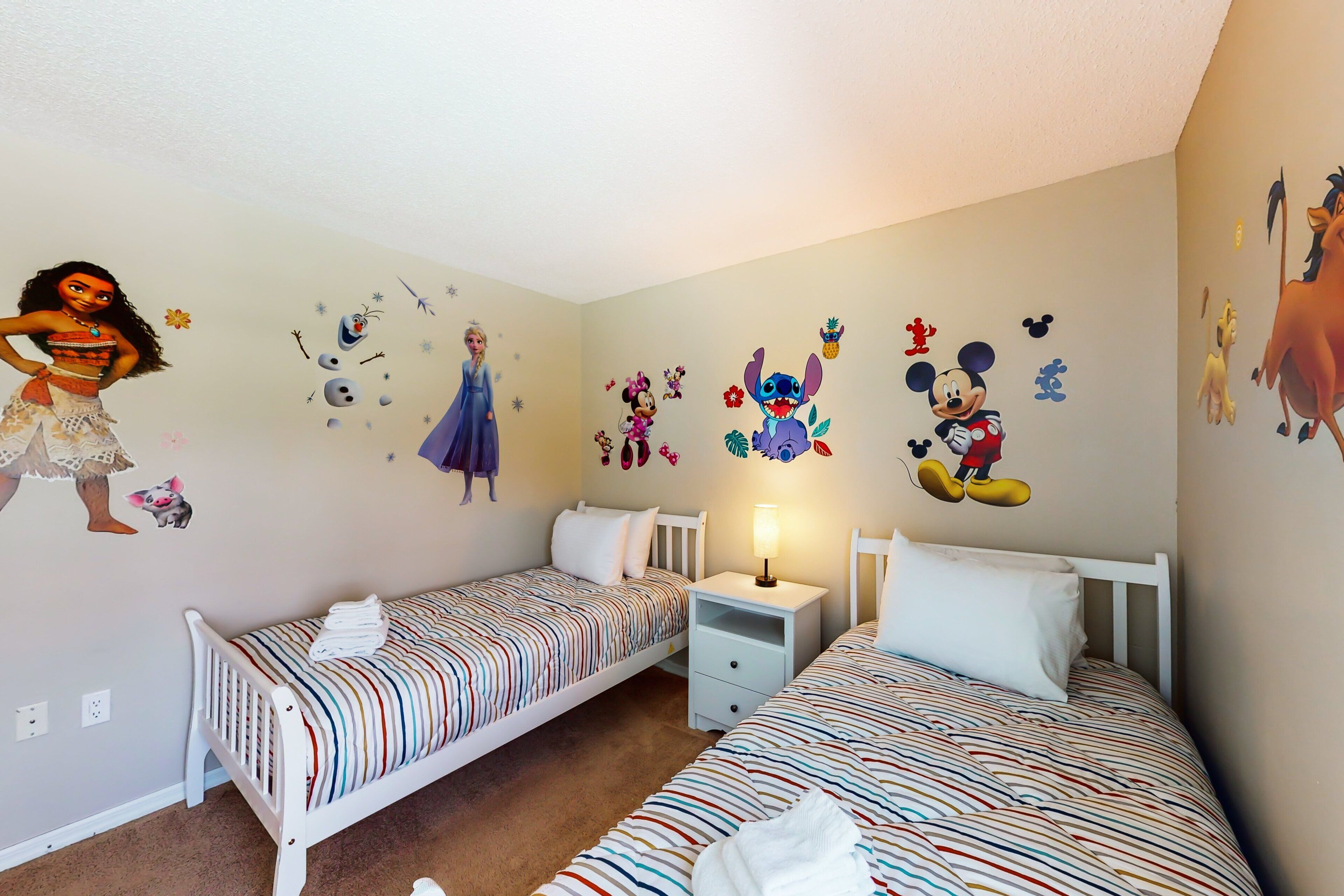 A children's room with two beds, a nightstand, and wall decals of animated characters.