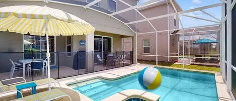 A pool area with lounge chairs, a striped umbrella, and a glass-enclosed building.