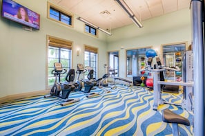 Ein Fitnessraum mit Trainingsgeräten, einem gemusterten Teppich und Fenstern mit Jalousien.