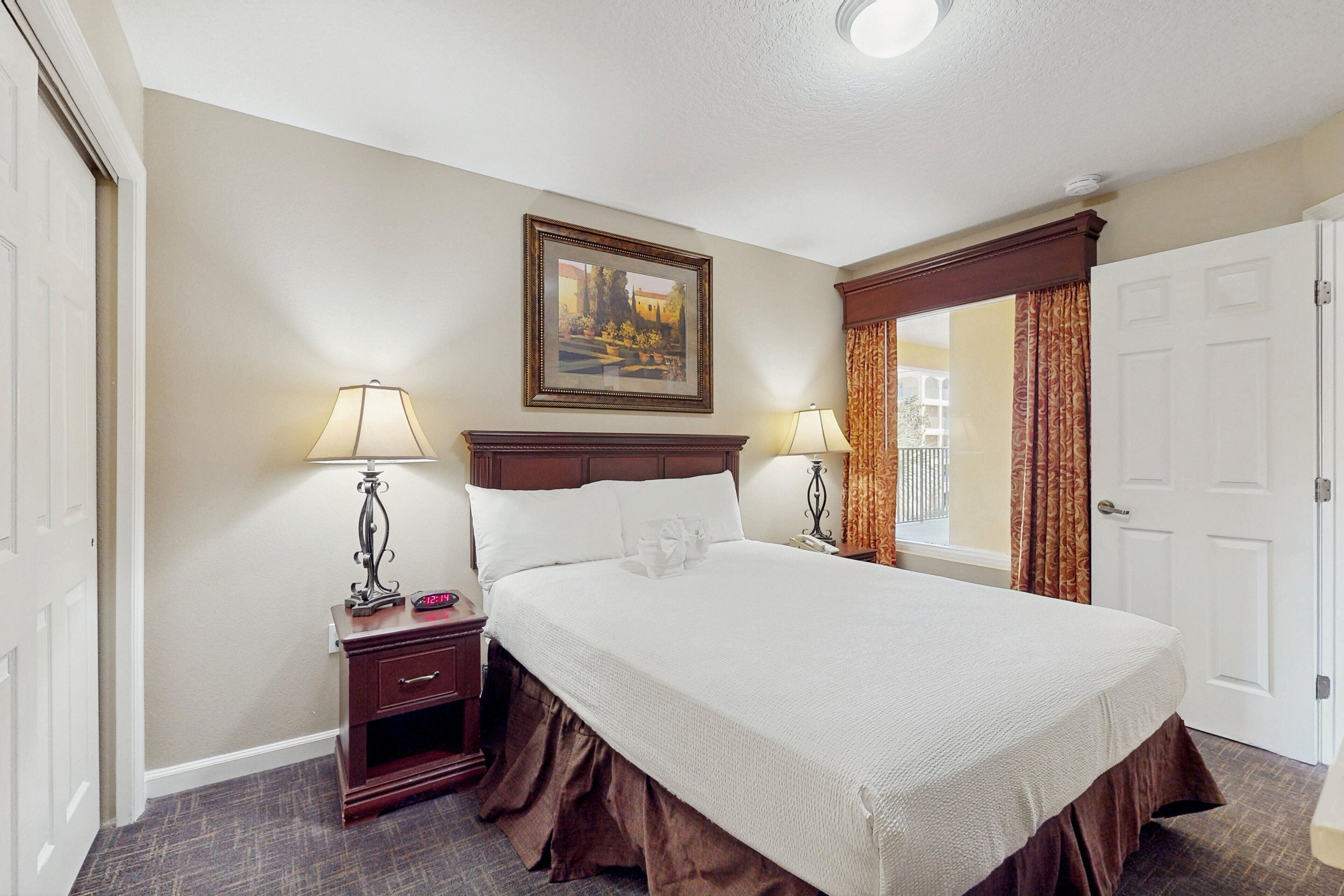Habitación de hotel con una cama grande, dos mesitas de noche con lámparas, un cuadro en la pared y una ventana con cortinas.