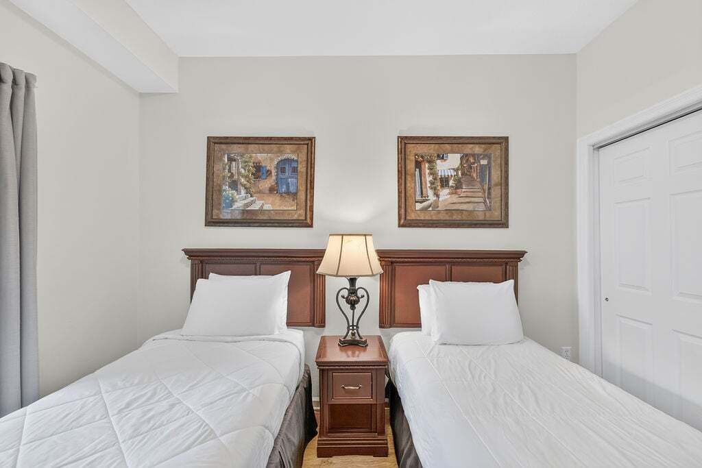 A hotel room with two beds, a nightstand with a lamp, and two framed pictures on the wall.