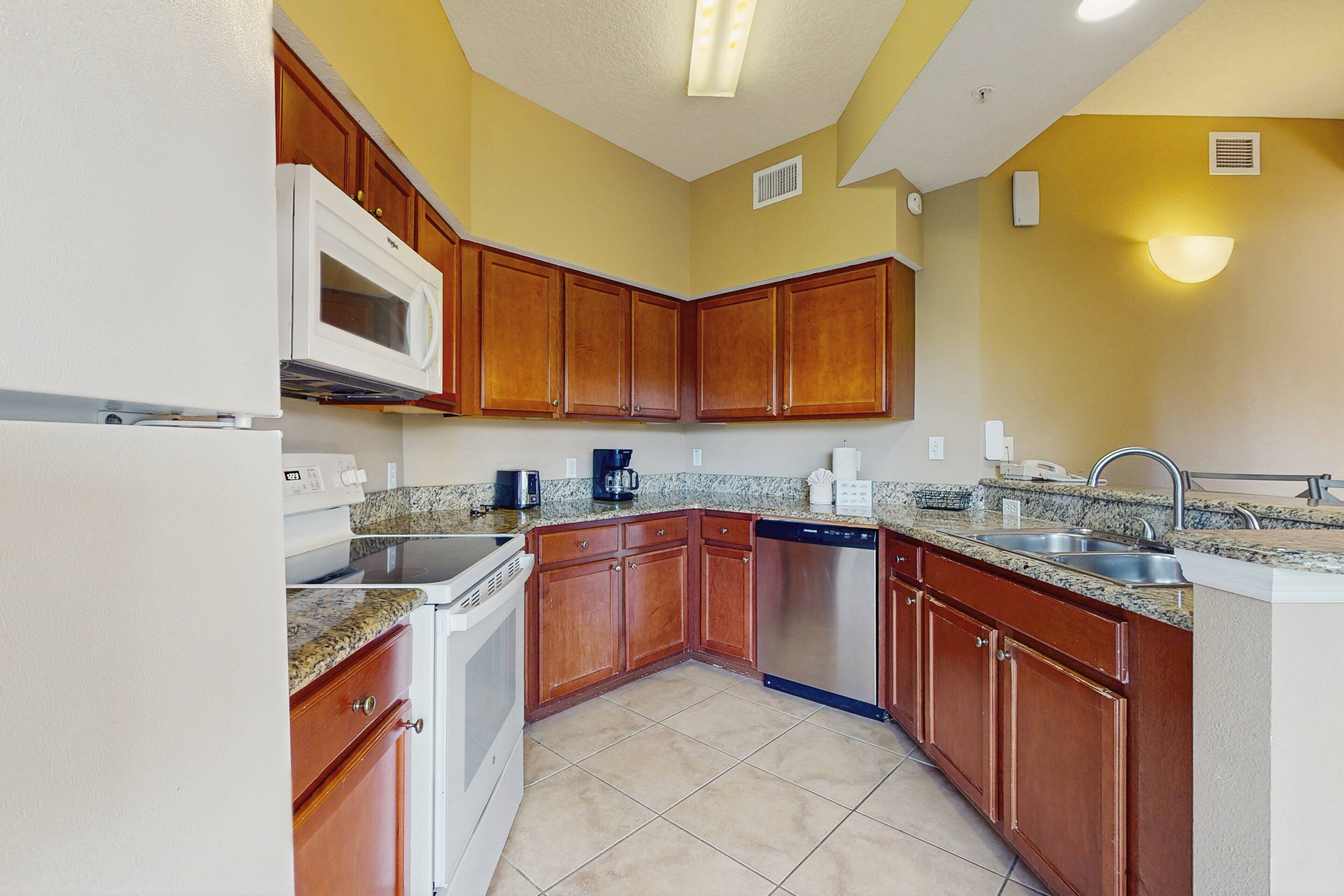 A kitchen with wooden cabinets, a microwave, a dishwasher, granite countertops, and a sink.