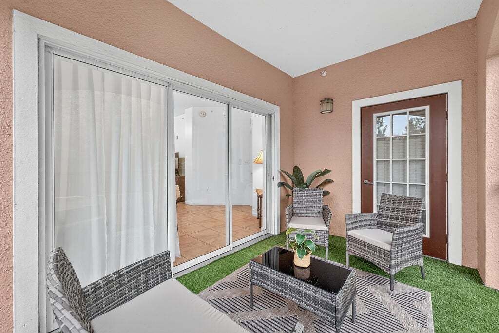 Een terras met rieten meubels, een glazen deur naar een kamer en een kleine tafel met een plant.
