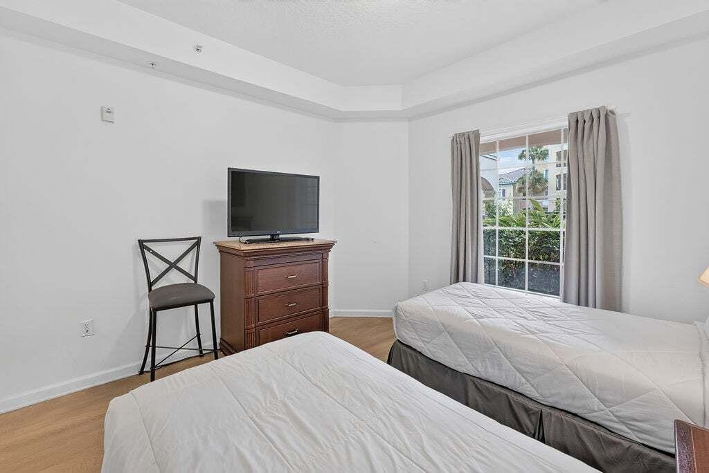 Una habitación con dos camas, un televisor sobre un tocador y una ventana con cortinas.