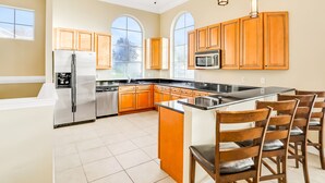 A spacious kitchen with a large island, wooden cabinets, stainless steel appliances, and a view through the windows. - Vibrant Modern Home With Private Pool, Spa, Lanai & Expansive Game Room (Haines City)