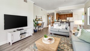 A modern living room with a flat-screen TV, a grey sofa, and a coffee table with decorative items. - Spacious and Inviting Getaway Condo Close to Disney and Universal (Kissimmee)