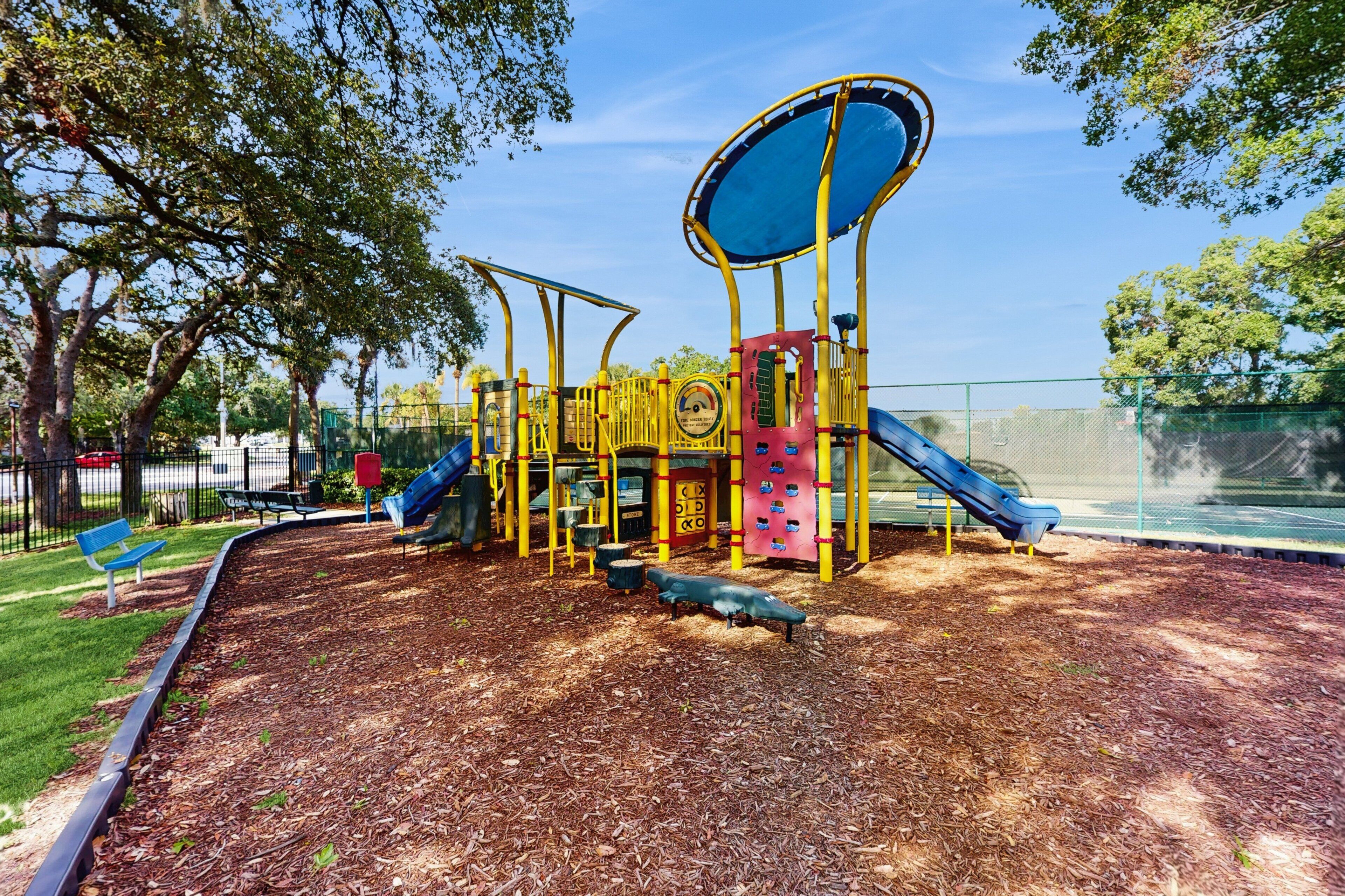A playground with slides and climbing structures, surrounded by trees and a fence.