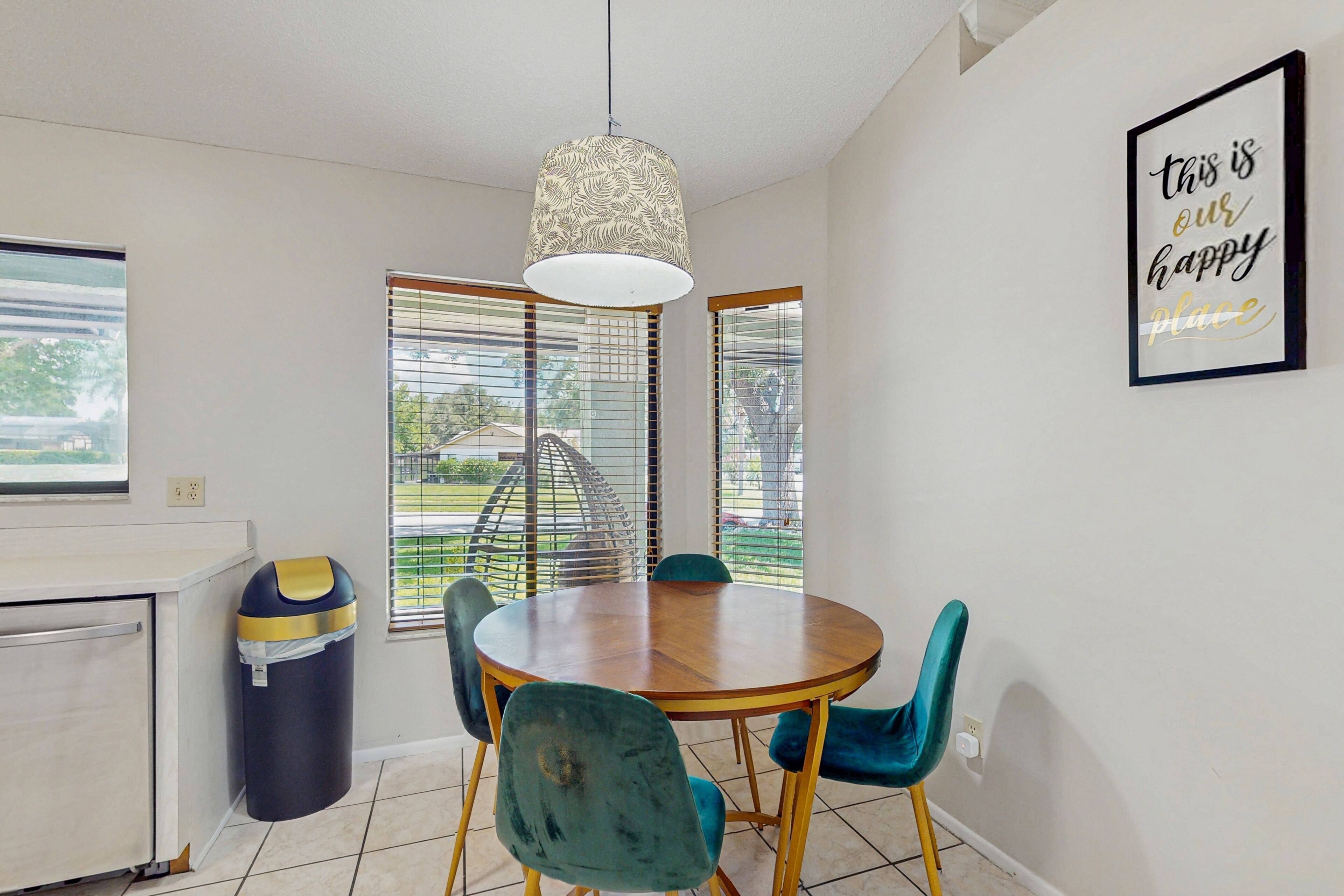 A dining area with a round wooden table, teal chairs, and a hanging light fixture.