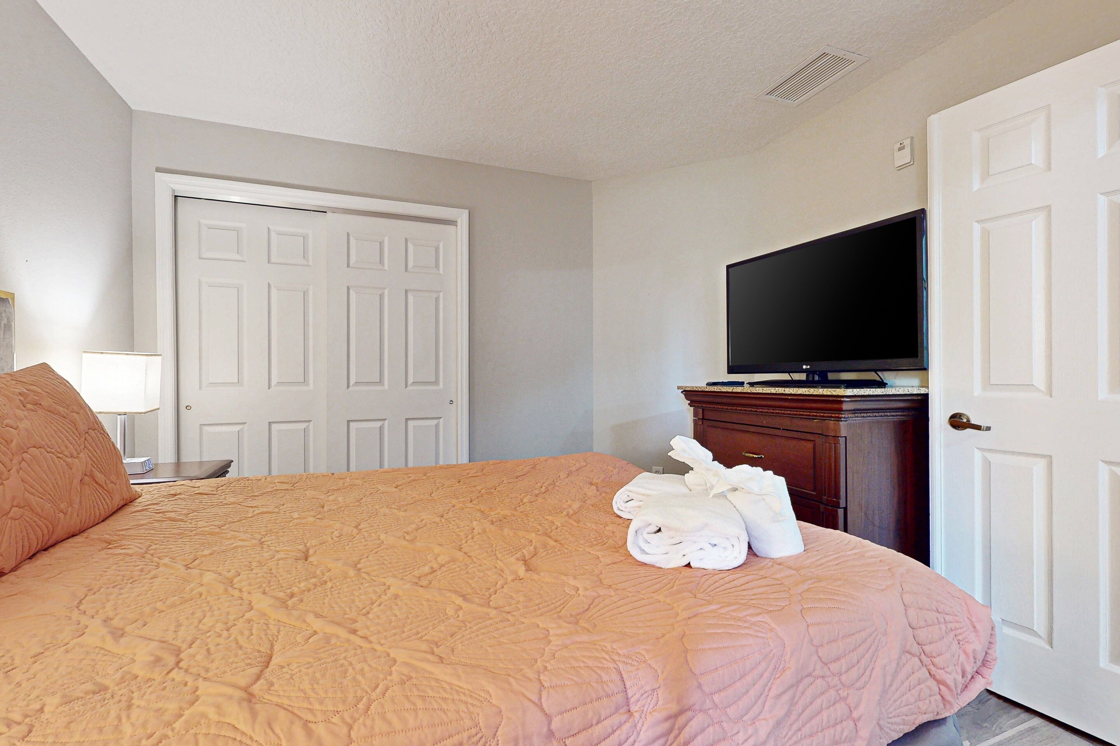 A hotel room with a bed, a television, a door, and a dresser.
