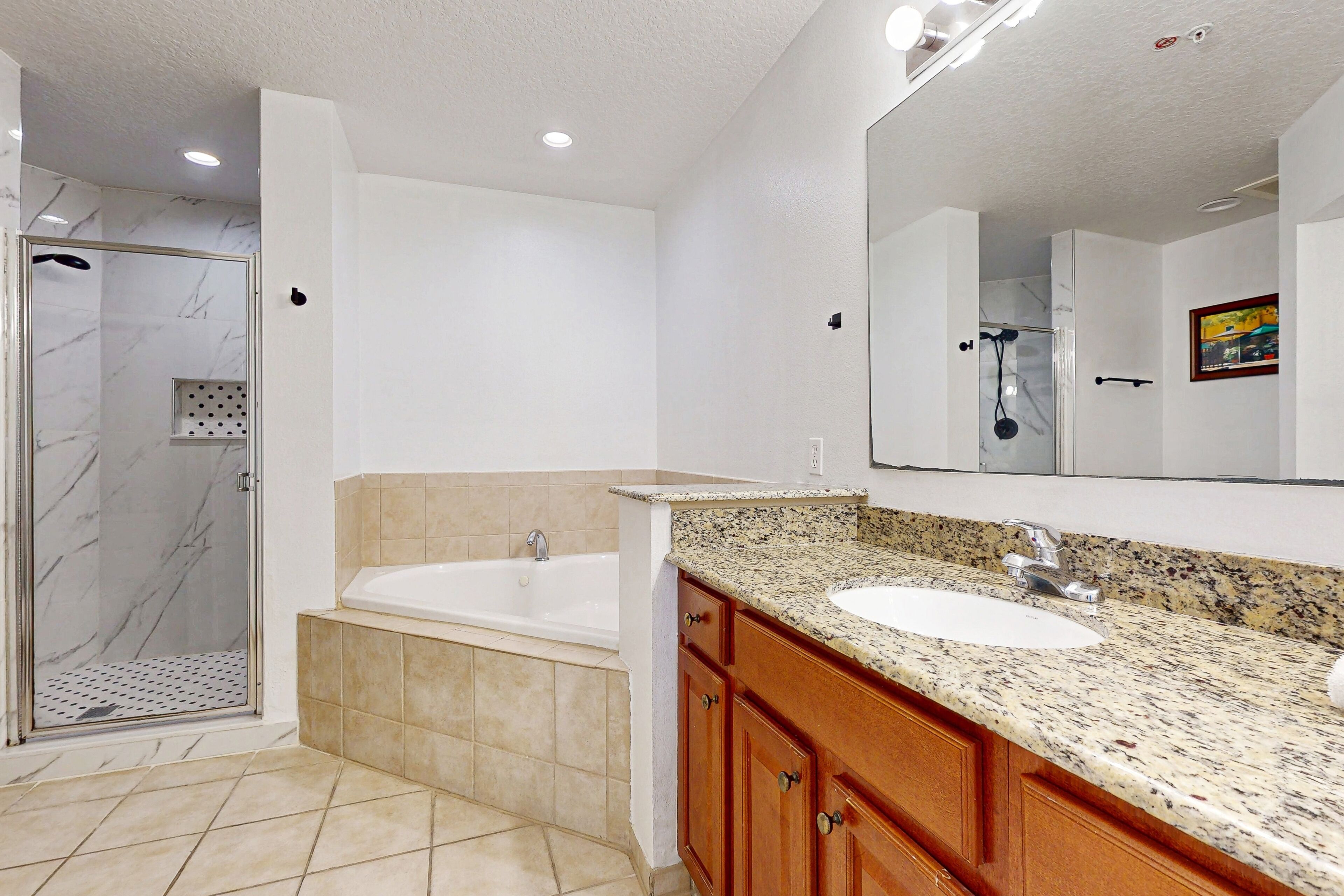 A modern bathroom with a glass-enclosed shower, a freestanding bathtub, and a granite countertop sink.
