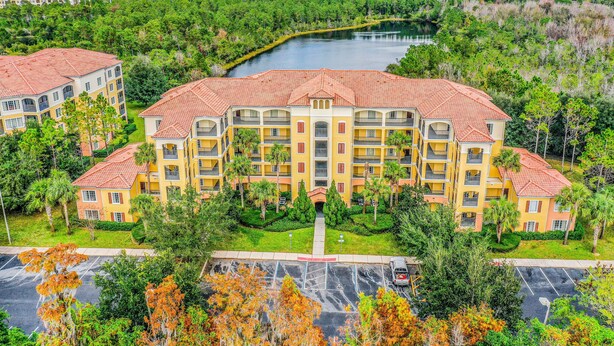 A multi-story hotel with a central courtyard, surrounded by lush greenery and a body of water. - Comfy Condo With Central AC, Wifi, Private Washer/dryer Minutes to Theme Parks (Orlando)