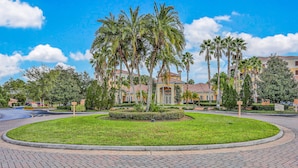 A landscaped area with palm trees, a paved walkway, and a building with a yellow facade. - Comfy Condo With Central AC, Wifi, Private Washer/dryer Minutes to Theme Parks (Orlando)