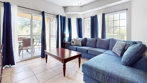 A spacious living room with a blue sofa, a wooden coffee table, and a ceiling fan. - Comfy Condo With Central AC, Wifi, Private Washer/dryer Minutes to Theme Parks (Orlando)