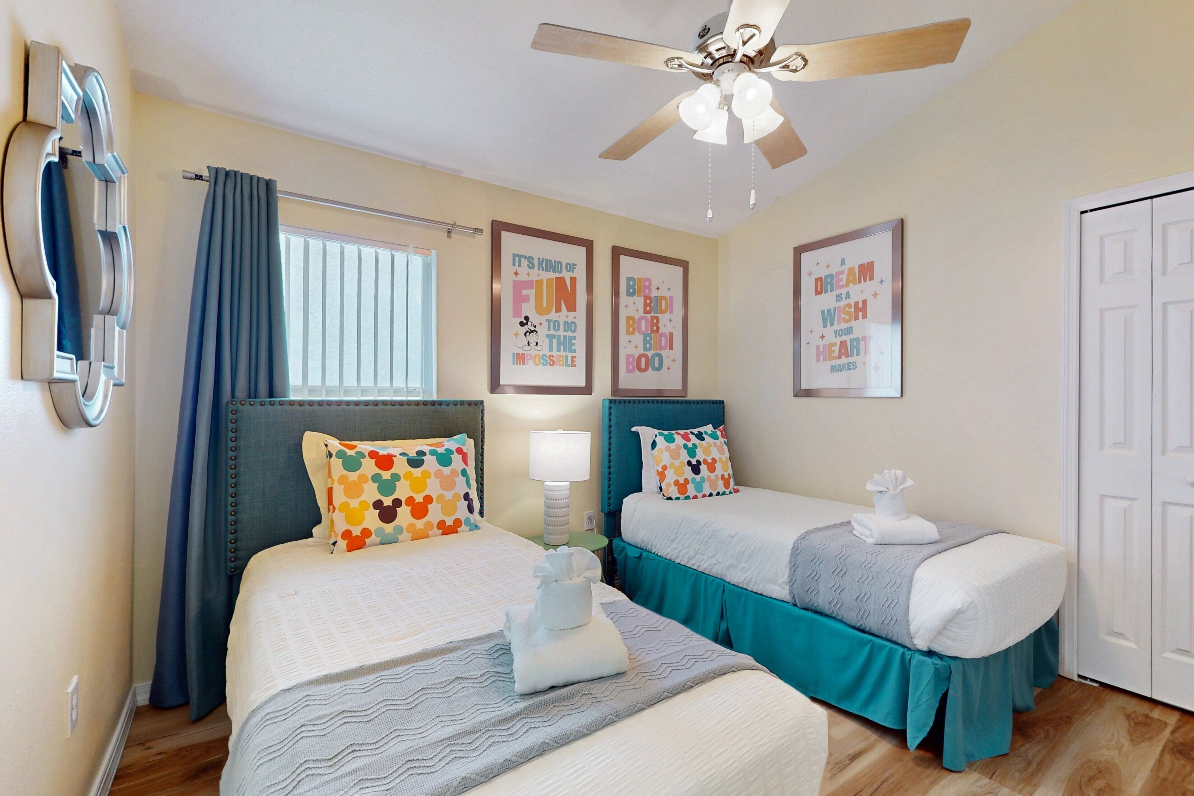 A hotel room with two beds, a ceiling fan, a window with curtains, and motivational posters on the wall.