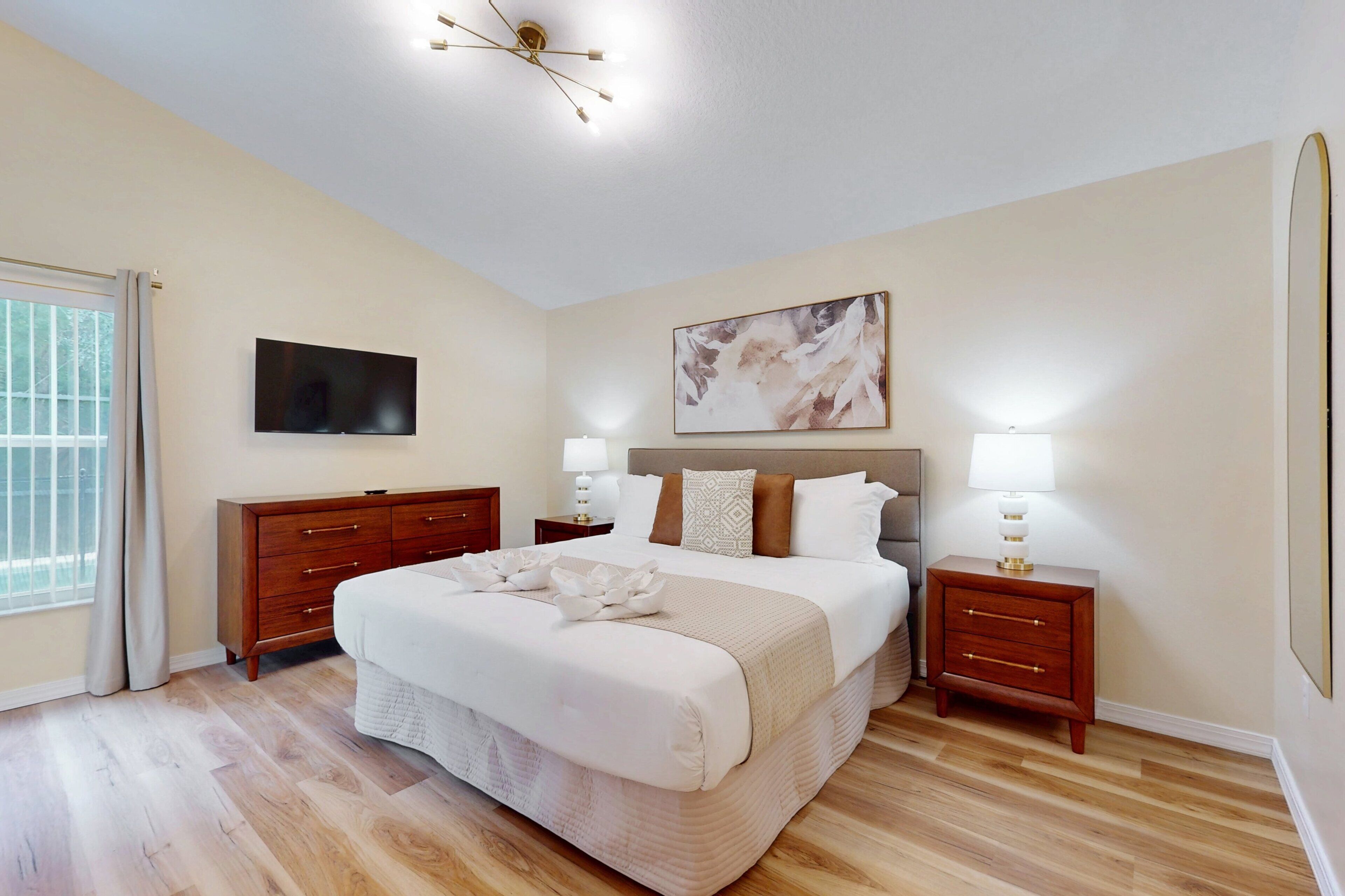 A bedroom with a large bed, a flat-screen TV, a painting, and a nightstand with a lamp.