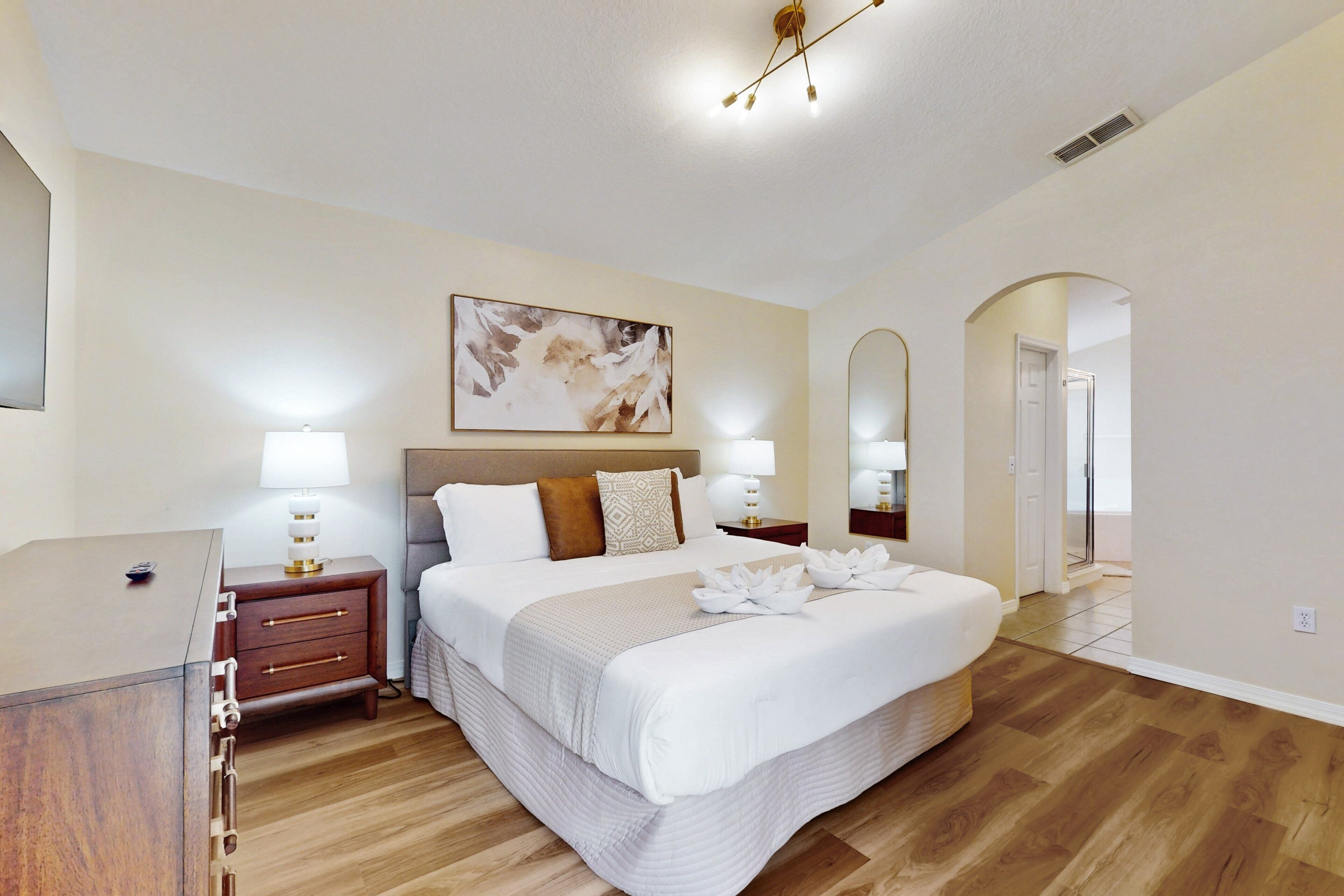 Una habitación de hotel con una cama grande, mesitas de noche con lámparas, un cuadro en la pared y un espejo.