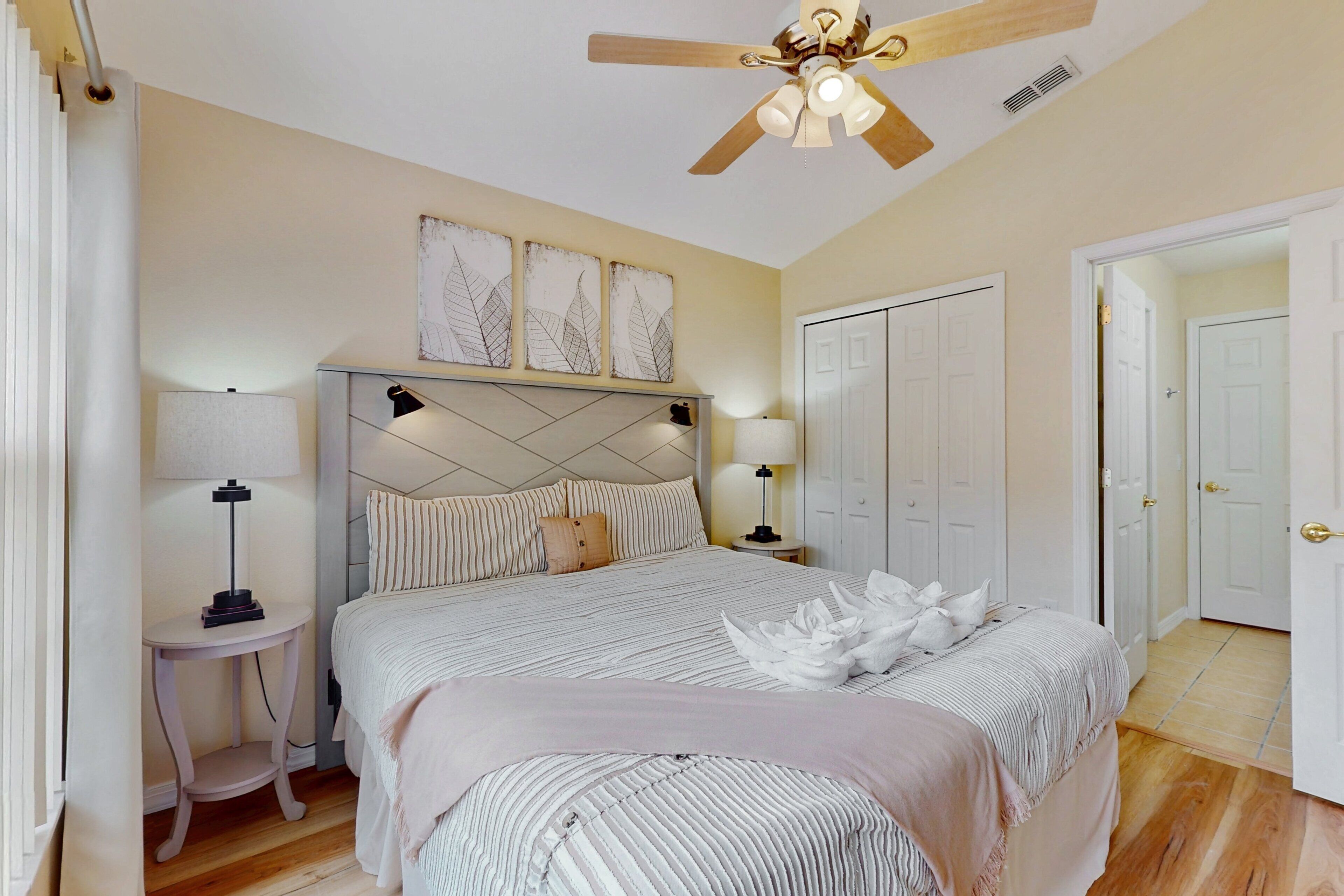 A bedroom with a bed, bedside tables, a ceiling fan, and a door.