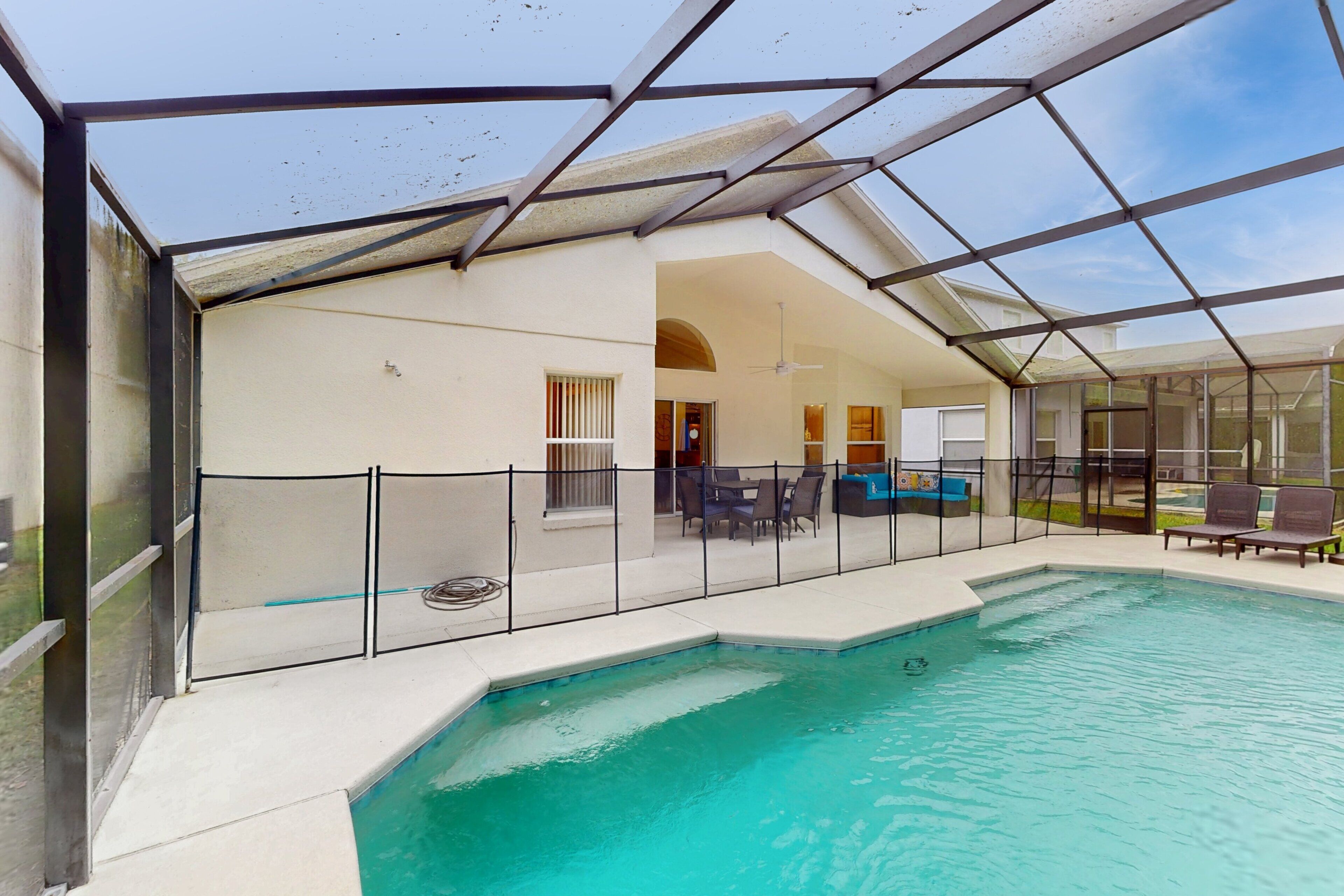 A swimming pool with a glass enclosure, outdoor furniture, and a clear sky.