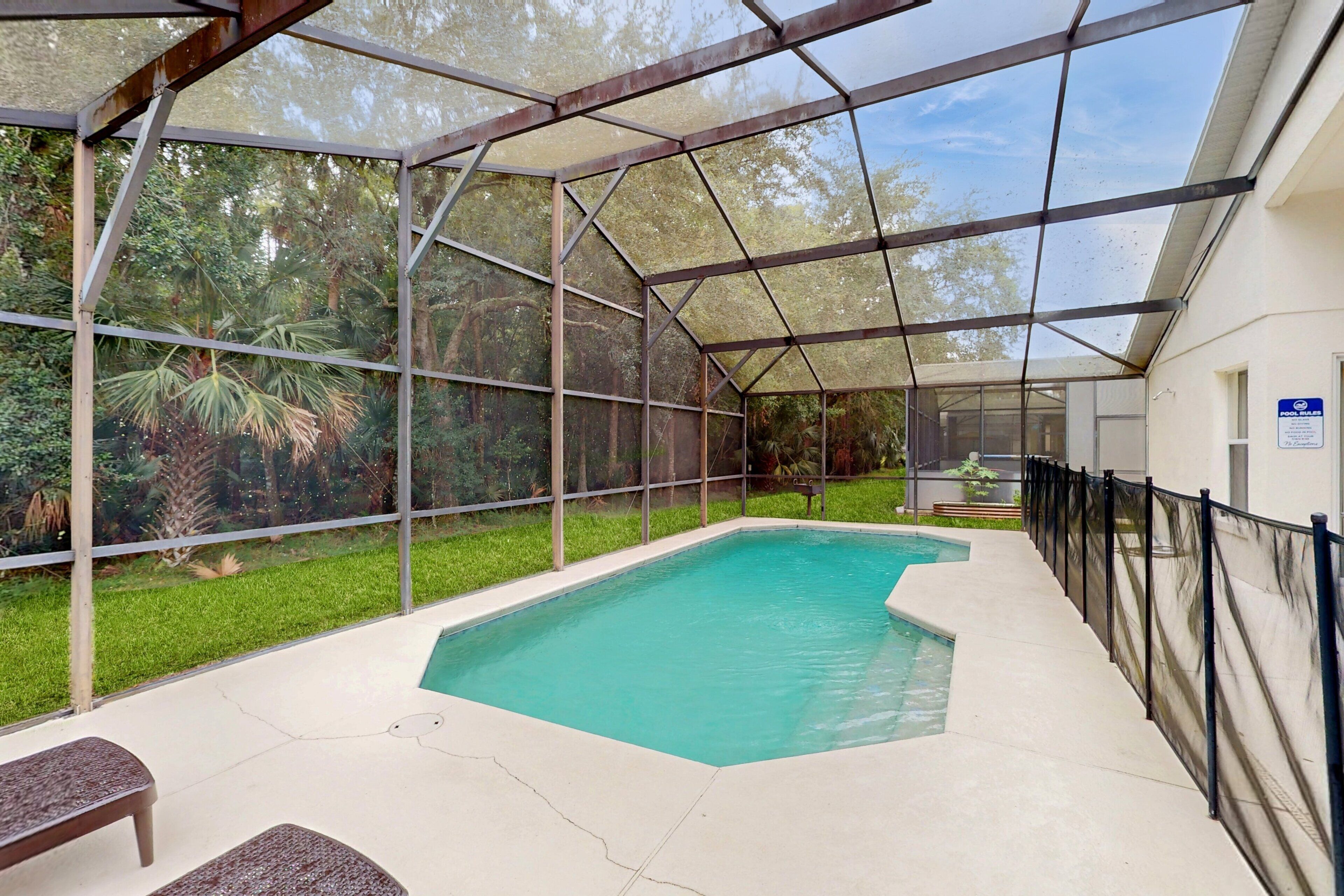 Una piscina exterior cubierta con techo metálico, bancos y zona verde con árboles.