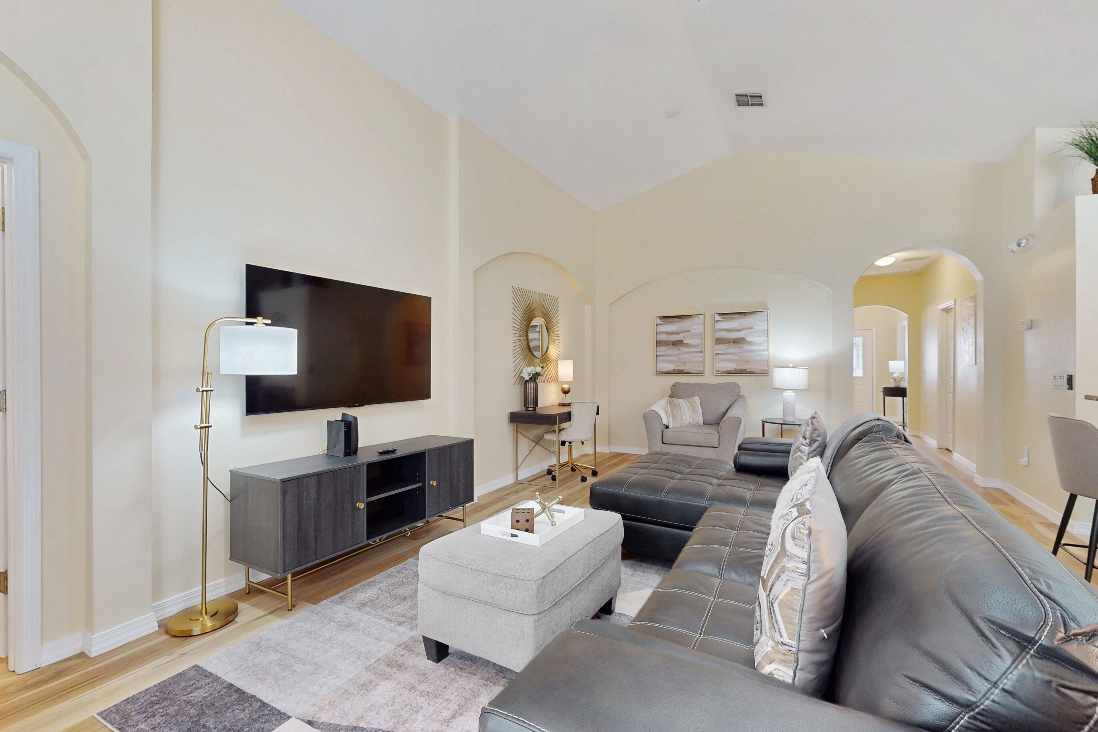 A modern living room with a large flat-screen TV, a grey sofa, a coffee table, and a floor lamp.