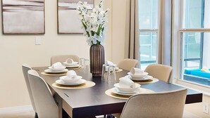 Comedor con mesa de madera oscura dispuesta para seis comensales, platos blancos y un florero con flores blancas.