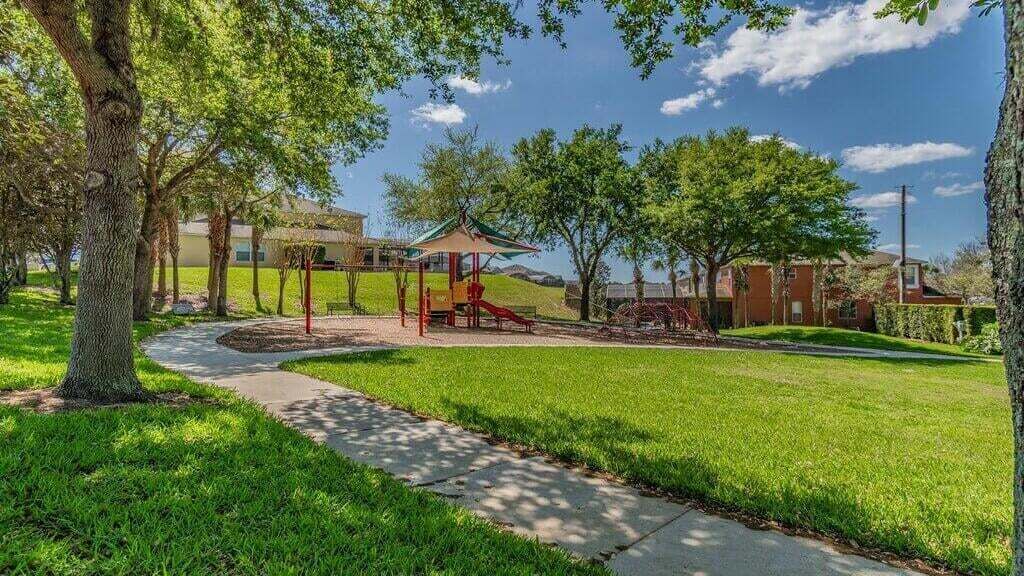 A playground with a slide and climbing structures, surrounded by grass and trees.