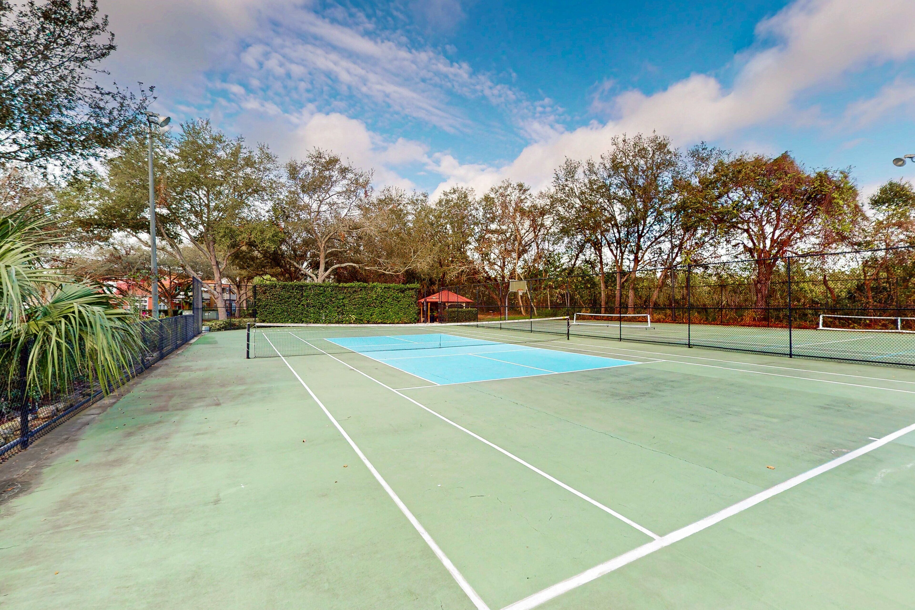 A tennis court with a net, surrounded by trees and a fence.
