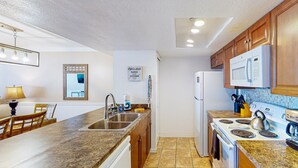 Una cocina con encimeras de granito, armarios de madera, microondas integrado, estufa y un fregadero.