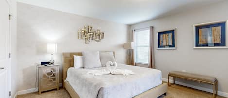 A bedroom with a bed, bedside table, lamp, artwork, and a bench.