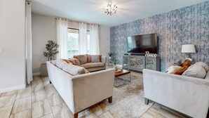 Een moderne woonkamer met een bank, fauteuils, een salontafel, een televisie en een behang met een patroon.