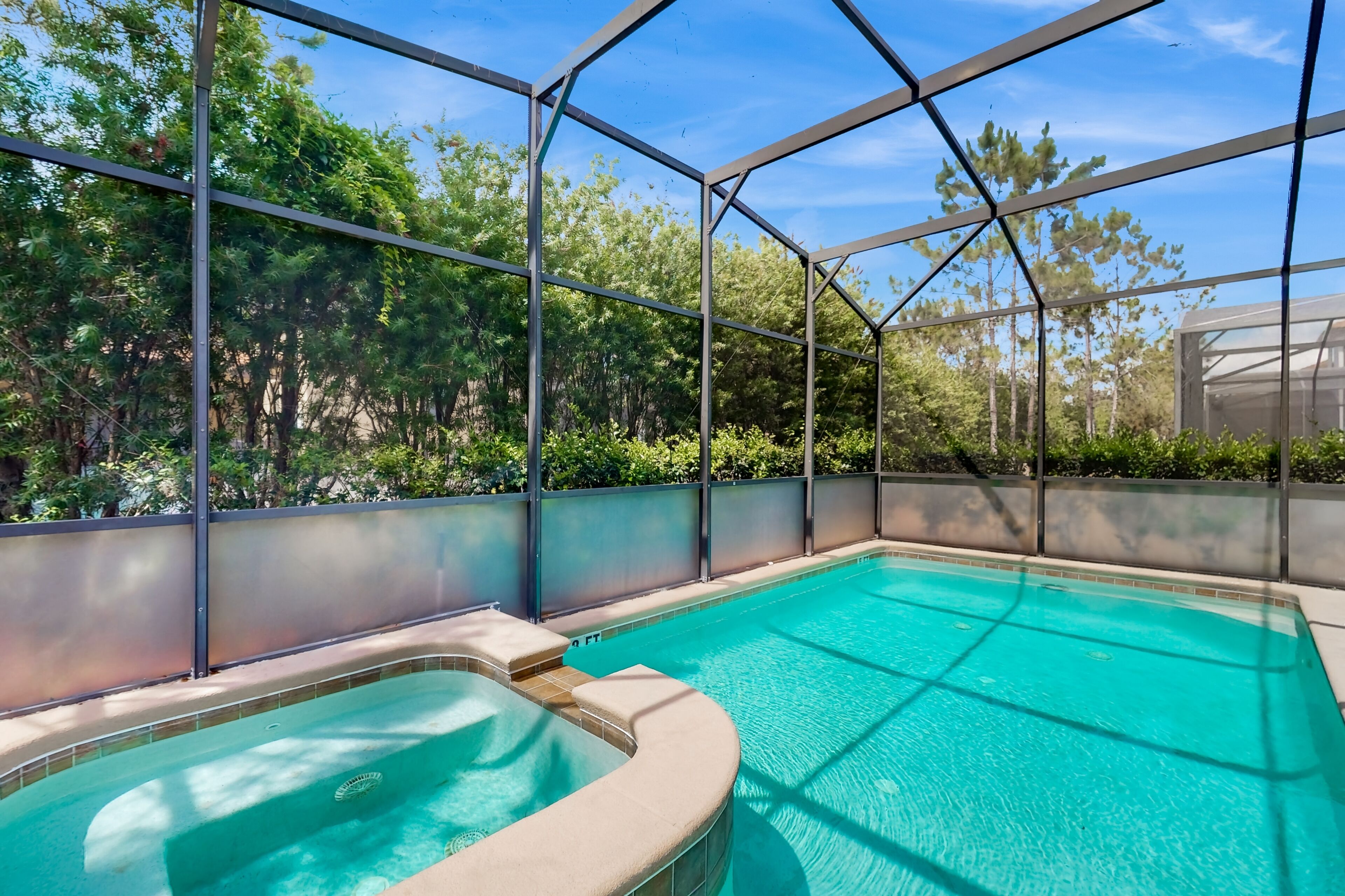 Une piscine avec un jacuzzi, entourée d’une clôture en métal et d’arbres.