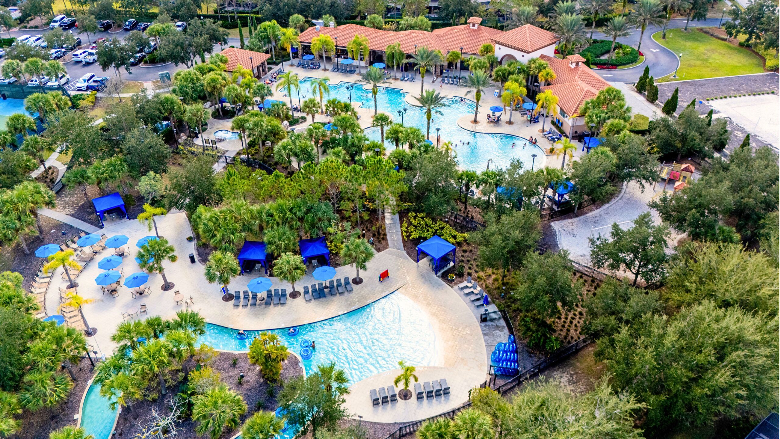 Eine Vogelperspektive zeigt einen luxuriösen Urlaubsort mit mehreren Schwimmbecken, Liegebereichen und Palmen.
